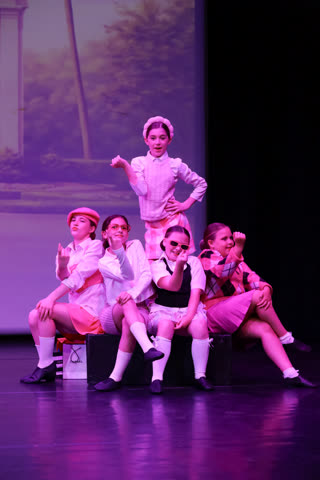 Group of pupils in coordinated pink costumes posing together during a musical theatre number
